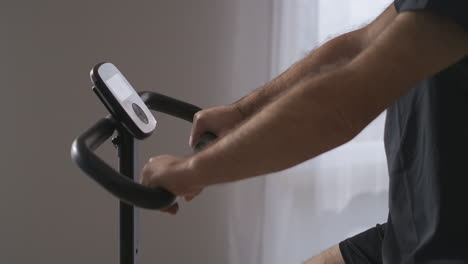 hands-of-adult-man-on-stationary-bicycle-during-training-at-home-details-shot-and-portrait-moving-shot-healthy-lifestyle-and-fitness